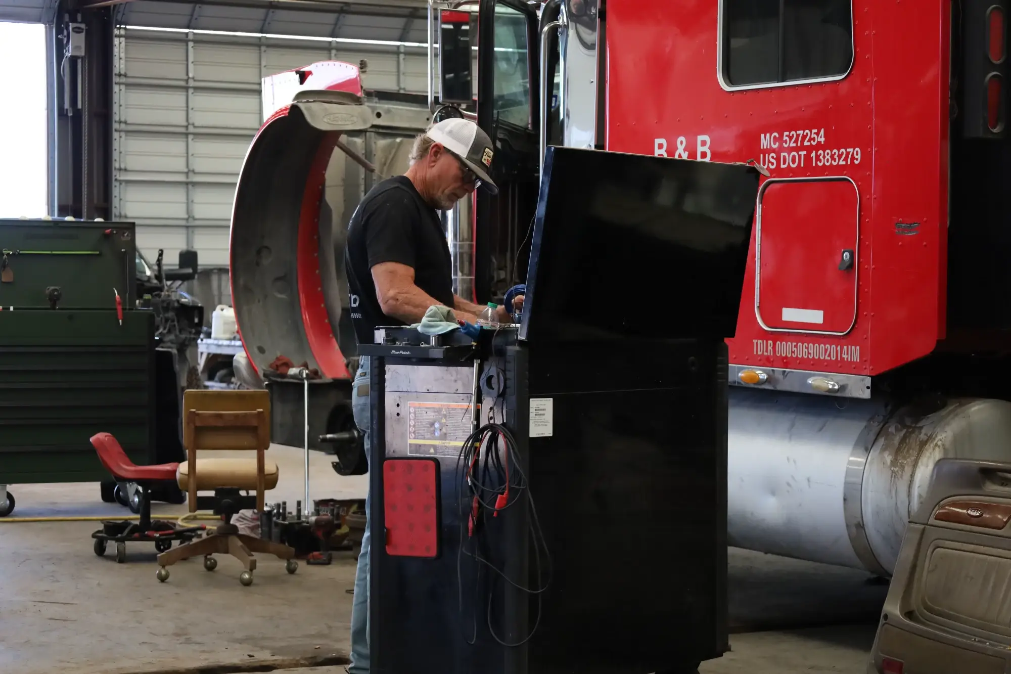 A mechanic works on a truck in a garage, specializing in gas and diesel vehicles, including heavy equipment fleets