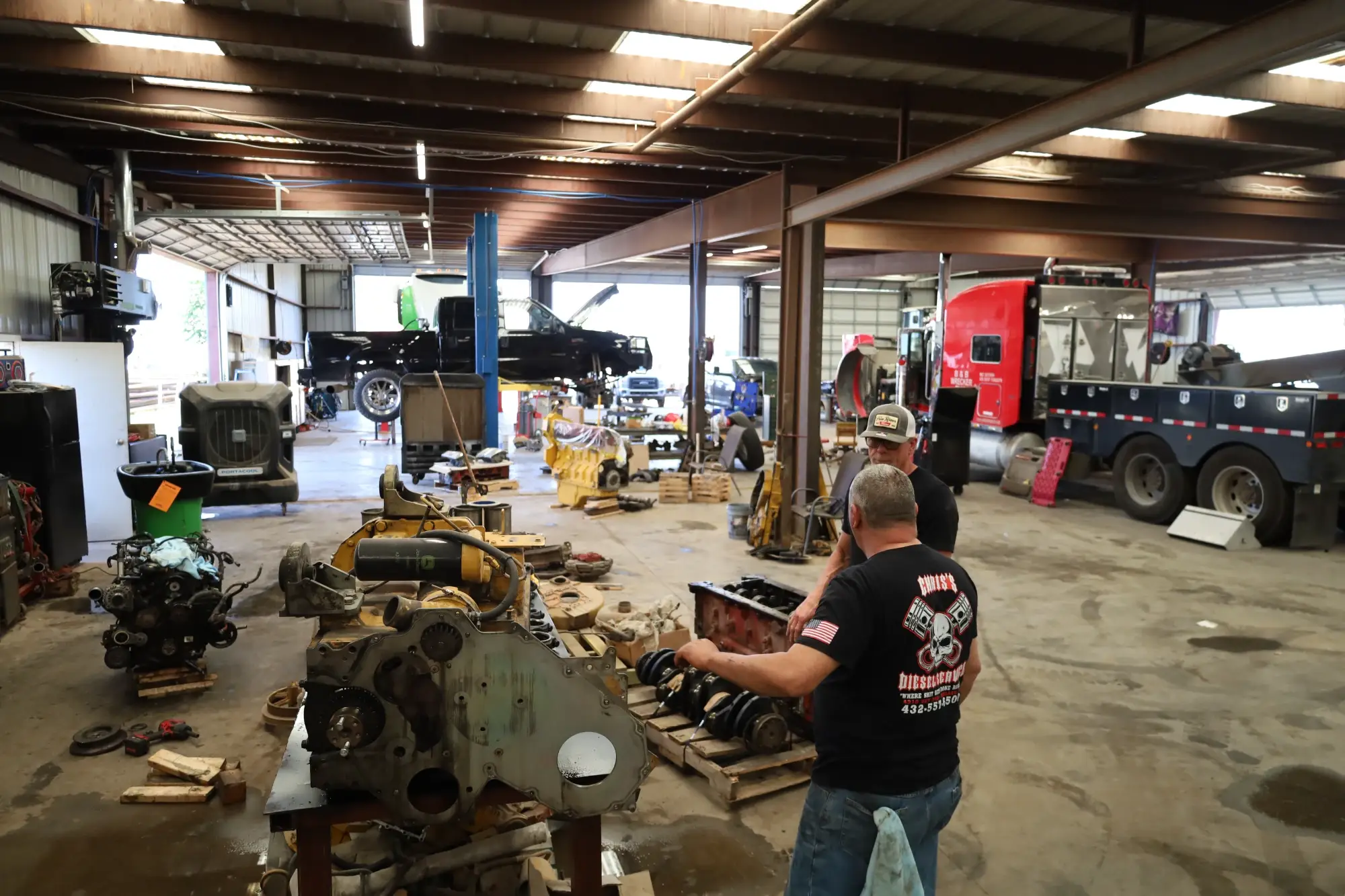 Technicians working on engines and components in a well-lit performance shop with industrial equipment