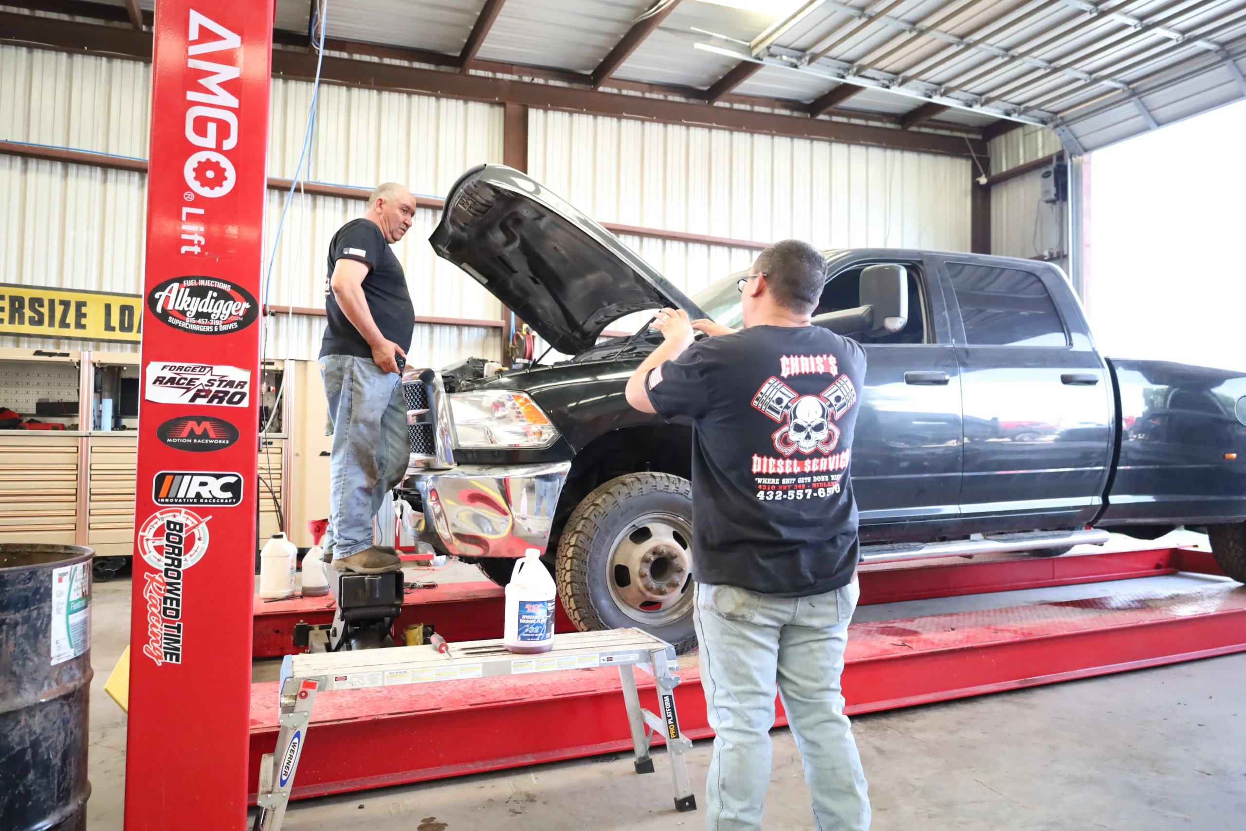Technicians performing truck oil change service using a hydraulic lift at Chris's Diesel Service in Midland TX