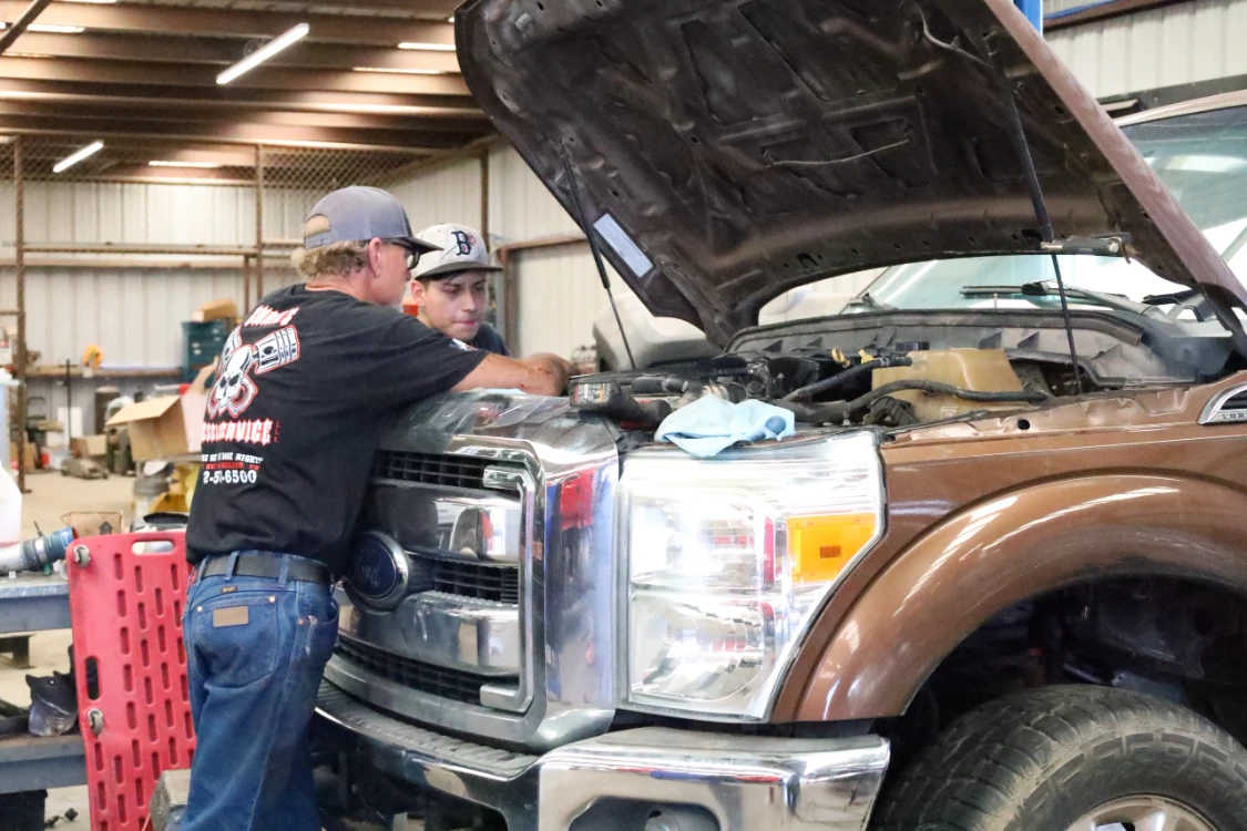 Diesel mechanic inspecting engine components on a Ford Super Duty truck at Chris's Diesel Service shop in Midland Texas