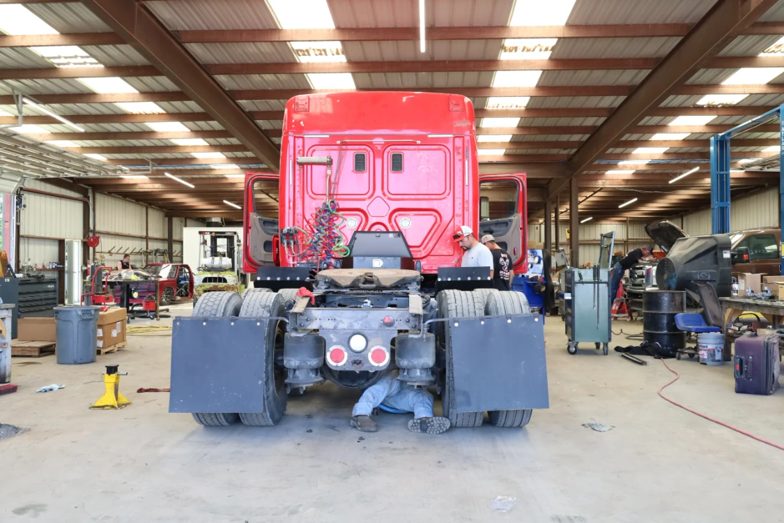 Diesel mechanic performing fleet truck repair under a red commercial semi truck at Chris's Diesel Service in Midland TX