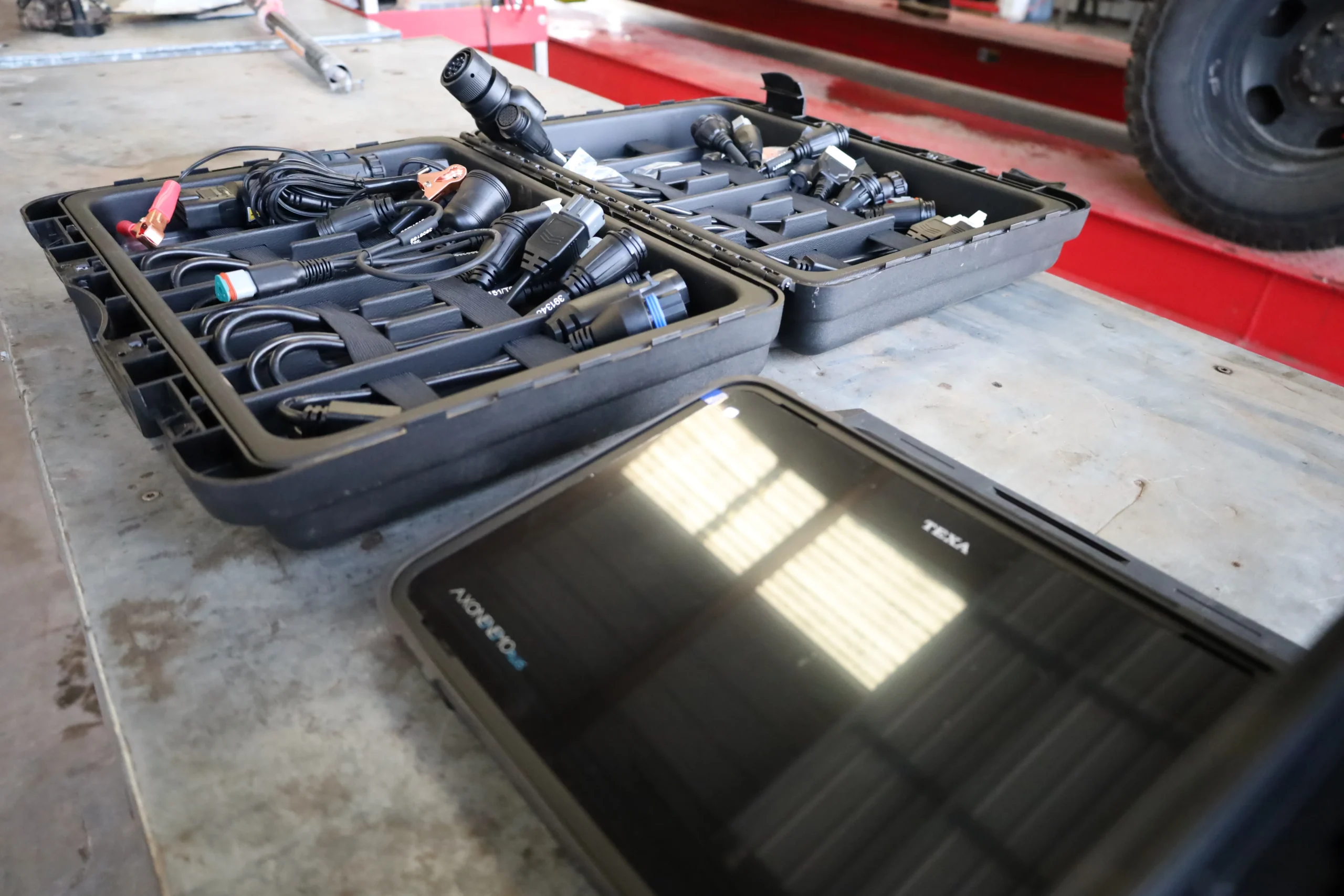 Electrical equipment including digital tablet scanner, OBD cables, and jumper cables in workshop setting