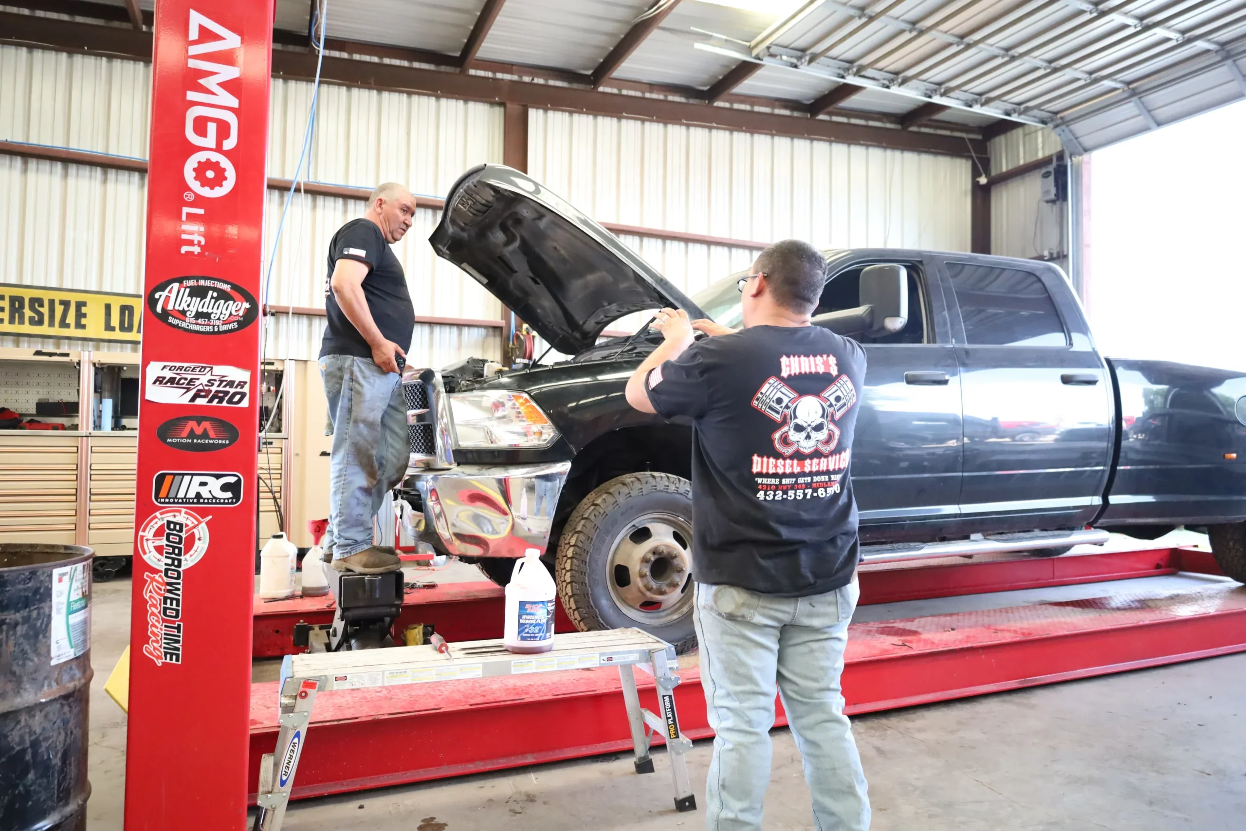 Technicians performing truck oil change service using a hydraulic lift at Chris's Diesel Service in Midland TX