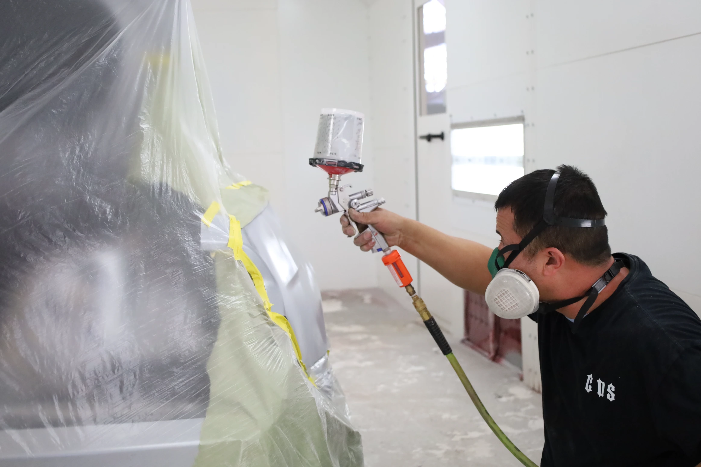Technician spray painting a vehicle panel in a paint booth at Chris's Diesel Service in Midland, TX