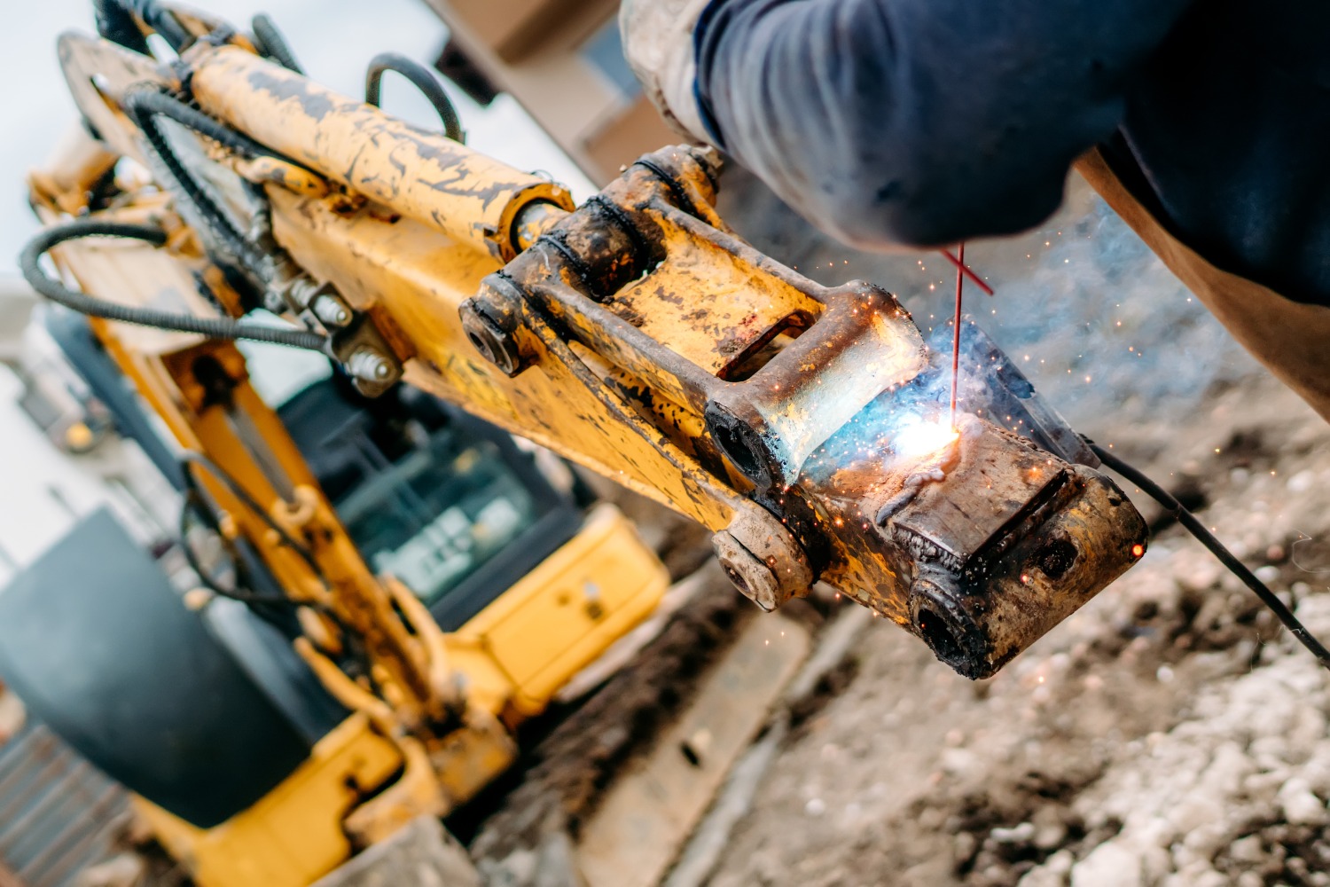 Welder repairing a cracked excavator boom arm with a MIG welding torch at the Midland shop